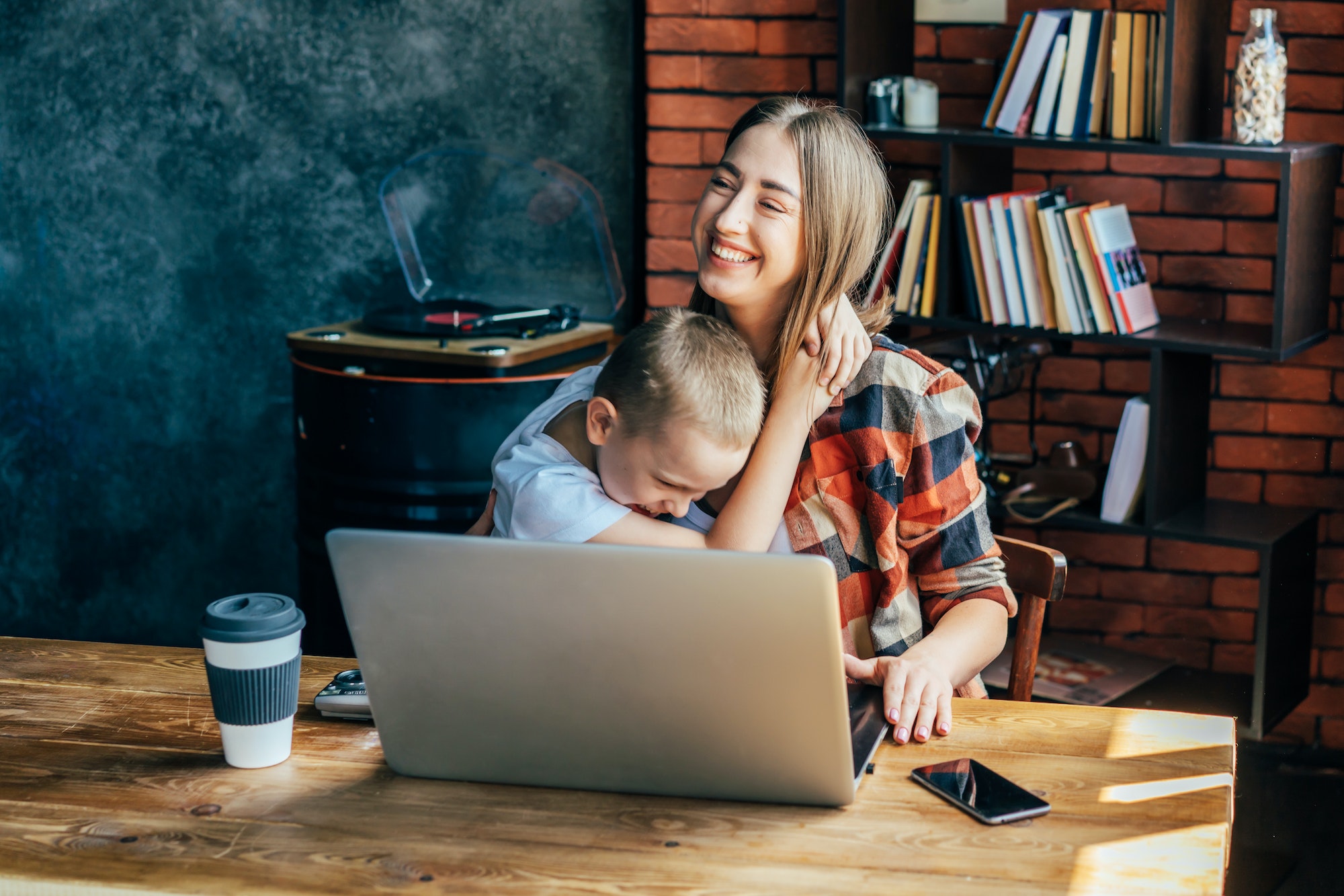 Mom and son laugh and hug, mom working from home. Student and teacher. (not a patient of ours that uses DENTAL IMPLANTS)